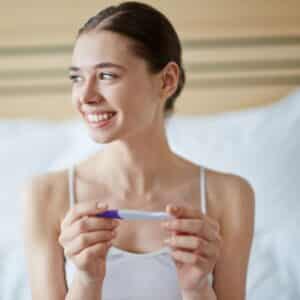 Mulher sorrindo ao segurar um teste de gravidez em suas mãos