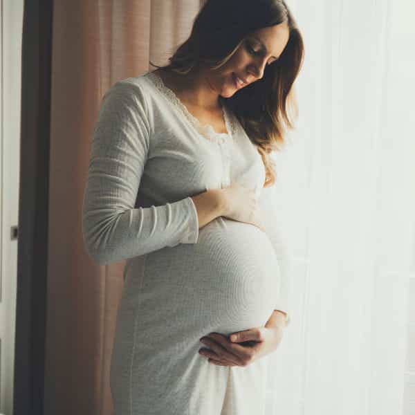 Close em mulher grávida passando a mão na barriga.