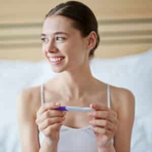Mulher sorrindo olhando para o lado com um teste de gravidez na mão
