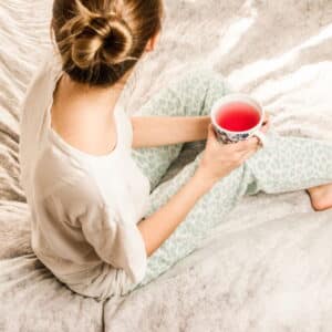Mulher sentada na cama segurando uma xícara com chá